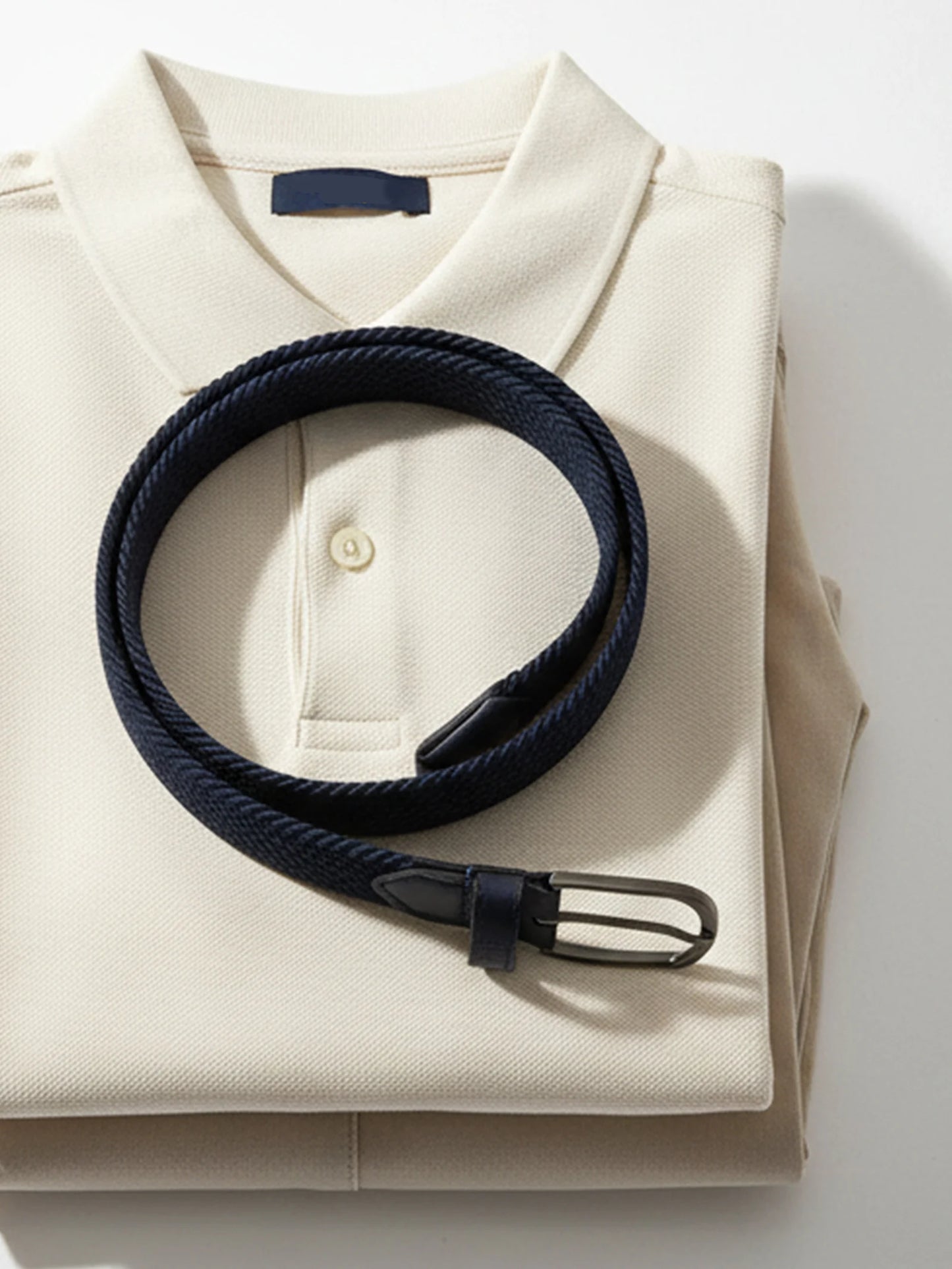 Folded beige shirt with a navy belt on a white background