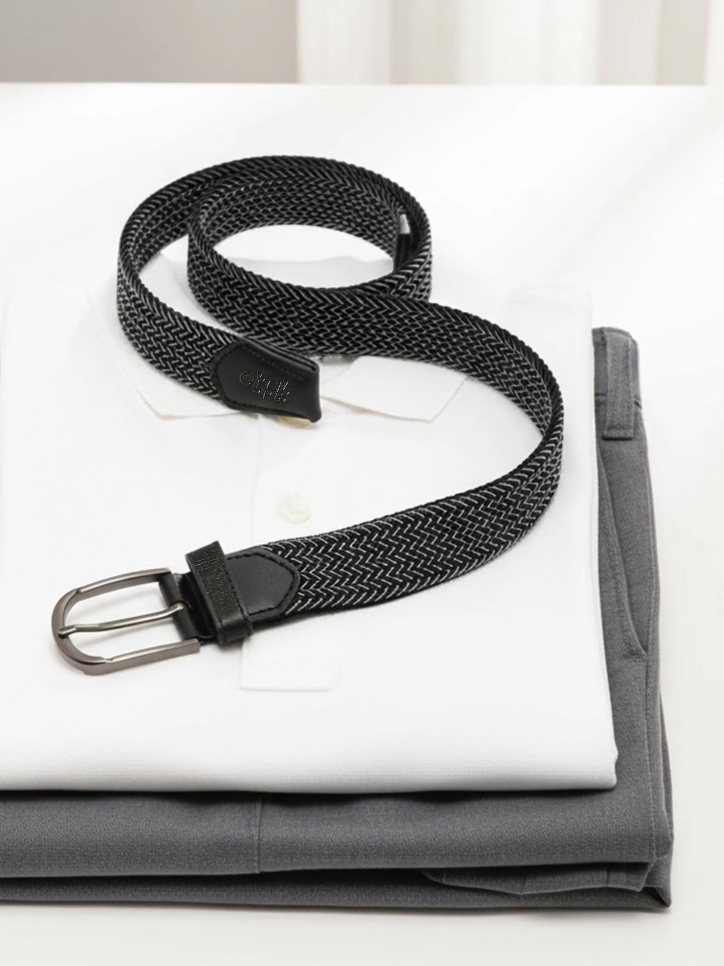Black woven belt with a silver buckle on a white shirt and gray fabric background