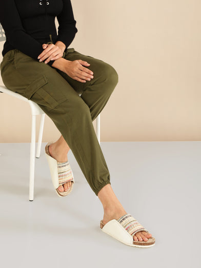 Person wearing olive green cargo pants sitting on a chair with a beige wall background