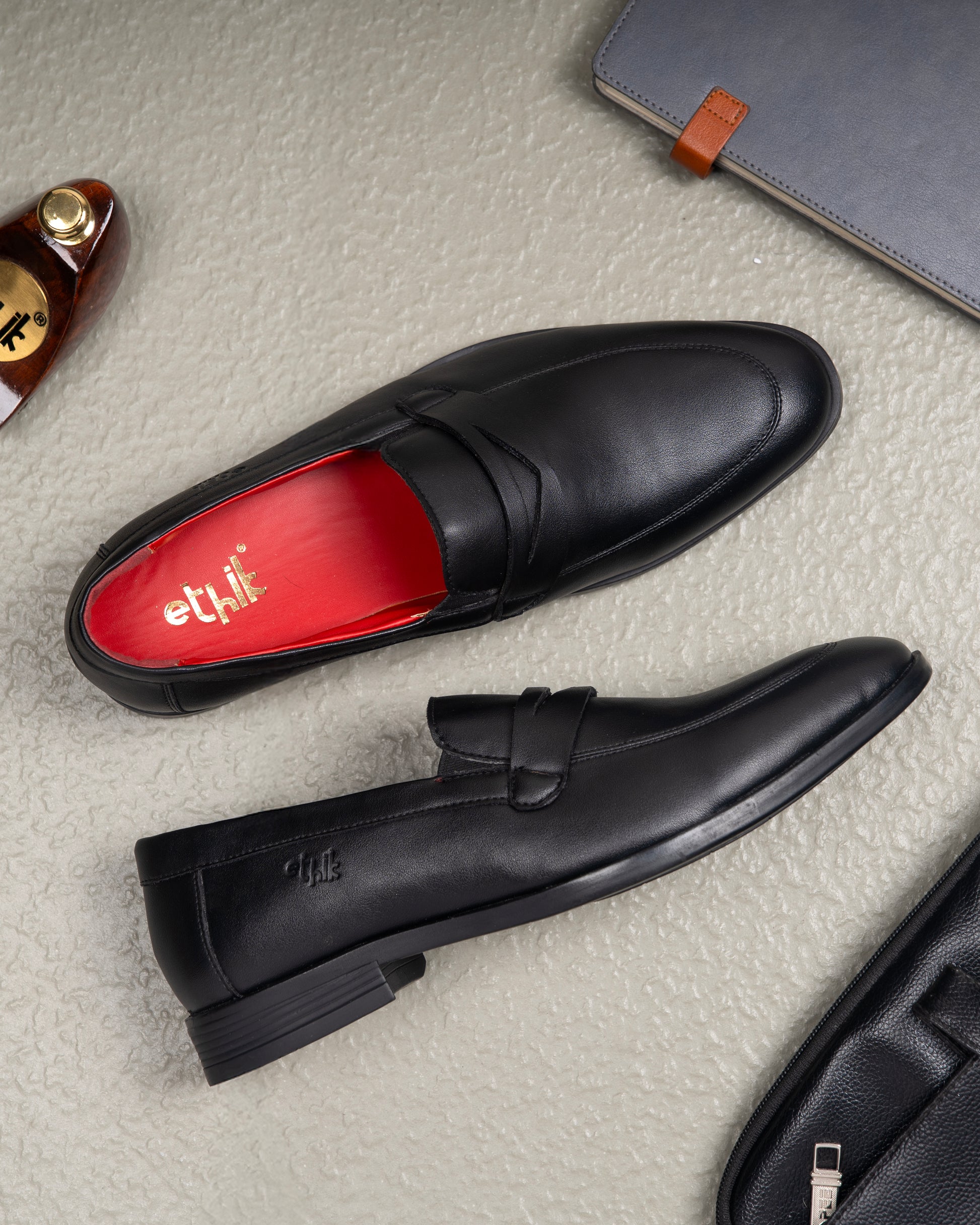 Black loafers with red lining on a textured surface