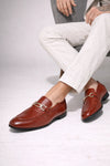 Brown leather loafers worn with white pants on a light gray background