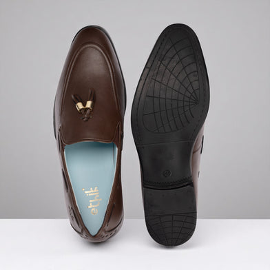 Brown loafer shoe with tassel on a gray background