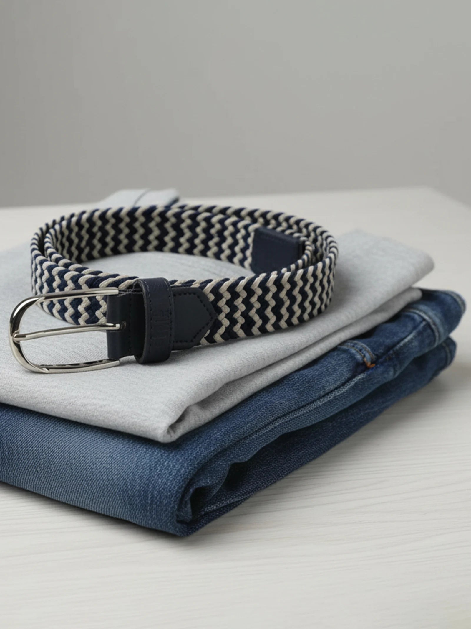 Folded jeans with a herringbone-patterned belt on a light surface