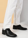 Black dress shoes worn with white pants on a neutral background